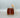 Glas mit rotbraunem, flüssigem Kastanienhonig und Holz-Honiglöffel vor grauem Hintergrund